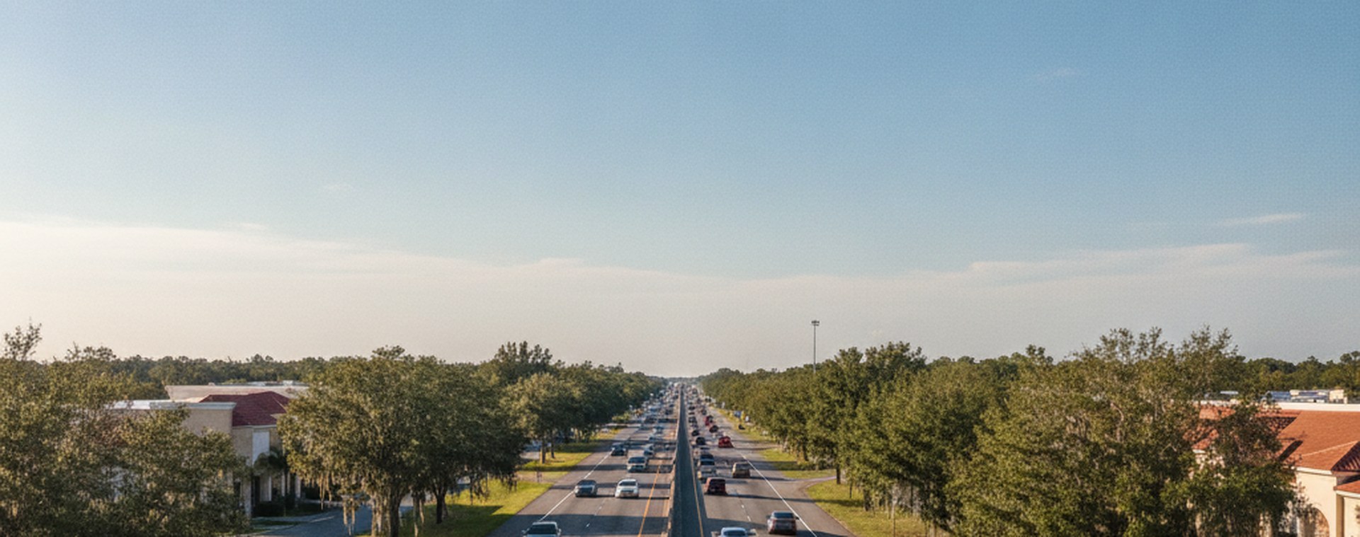 A Florida interstate seen from an overpass in afternoon light, ordinary traffic and live oaks alongside